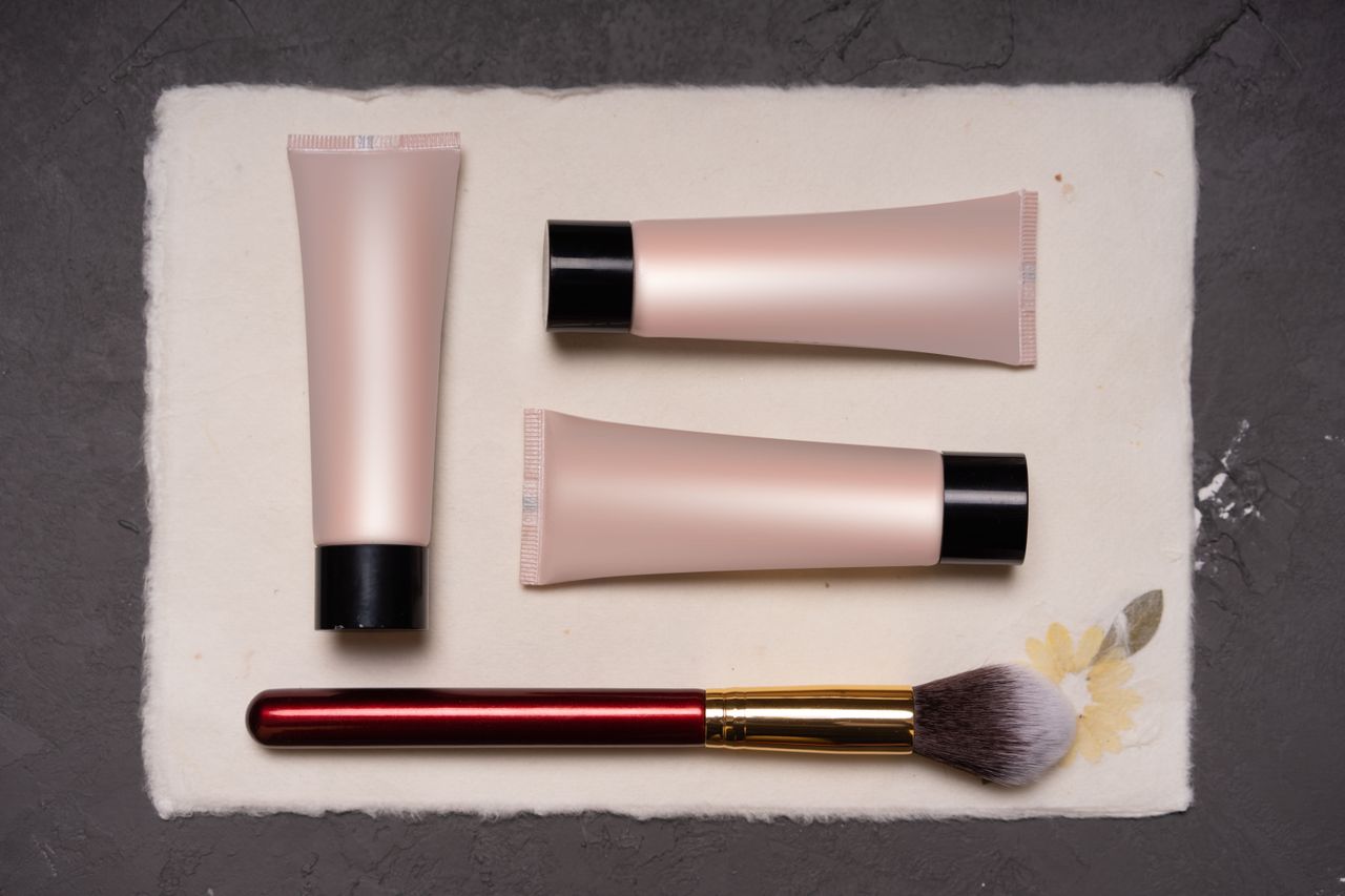 About Beauty composition featuring cosmetic tubes and a makeup brush on a textured background.