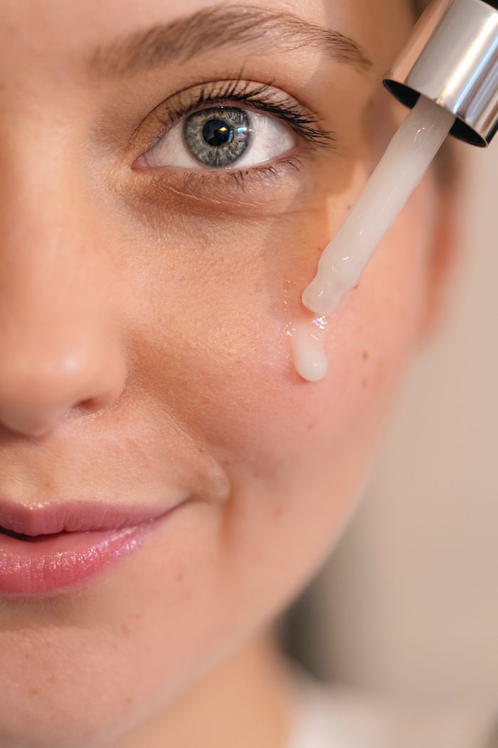 Services Close-up of a woman's face with serum dropper applying skincare product for healthy skin.