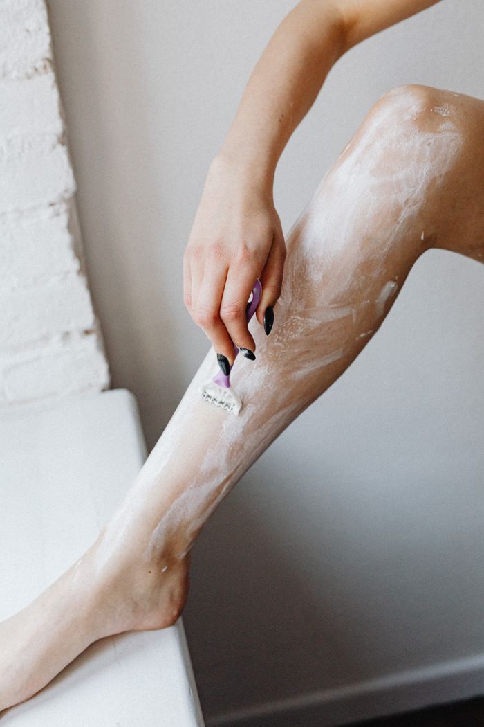 Woman shaving her leg with foam using a razor, showcasing personal grooming.